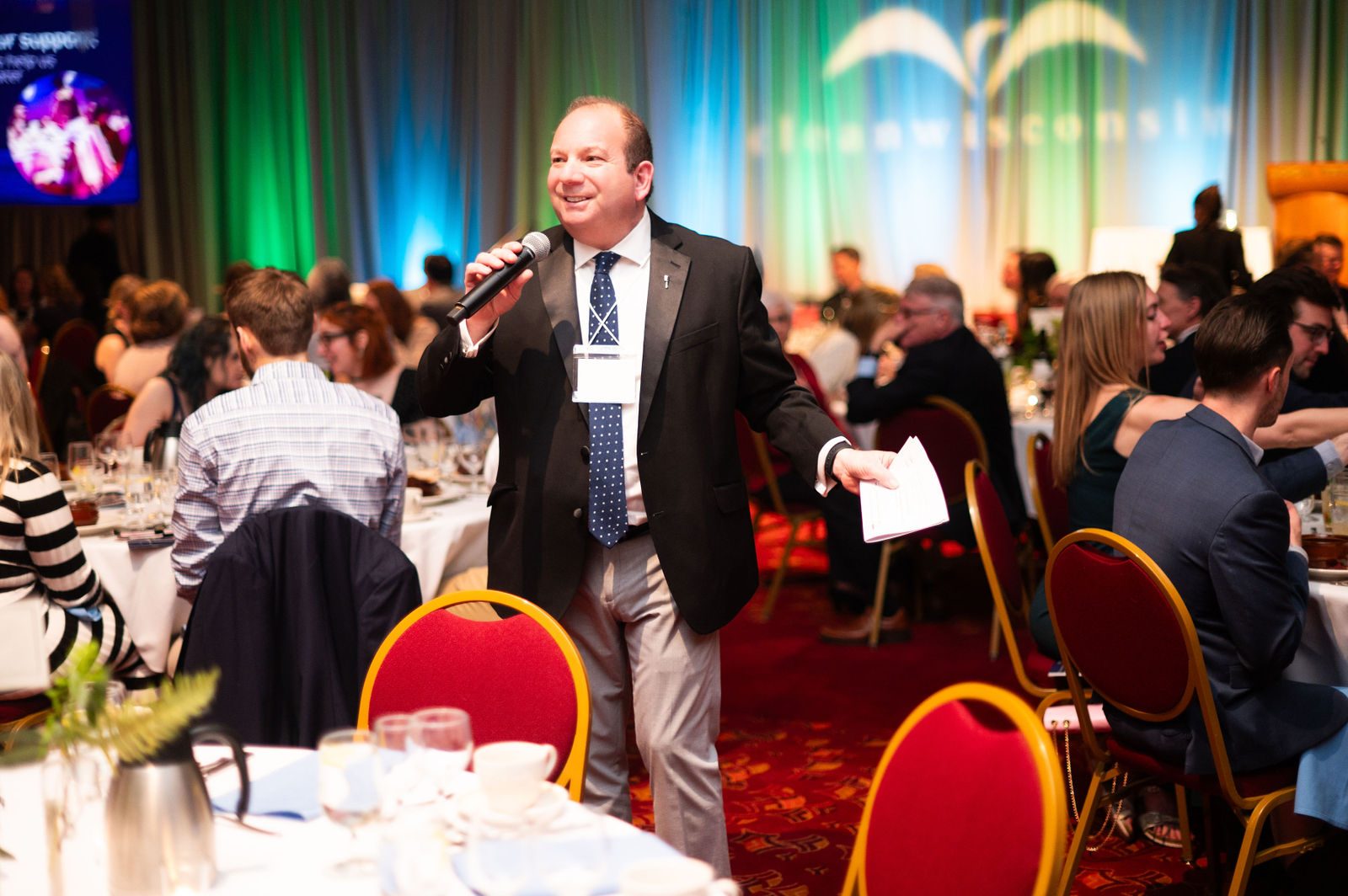 Benefit auctioneer Geoffrey Sandler on the microphone, walking among the tables of a full ballroom at Clean Wisconsin's Epicurean Evening at Monona Terrace in Madison