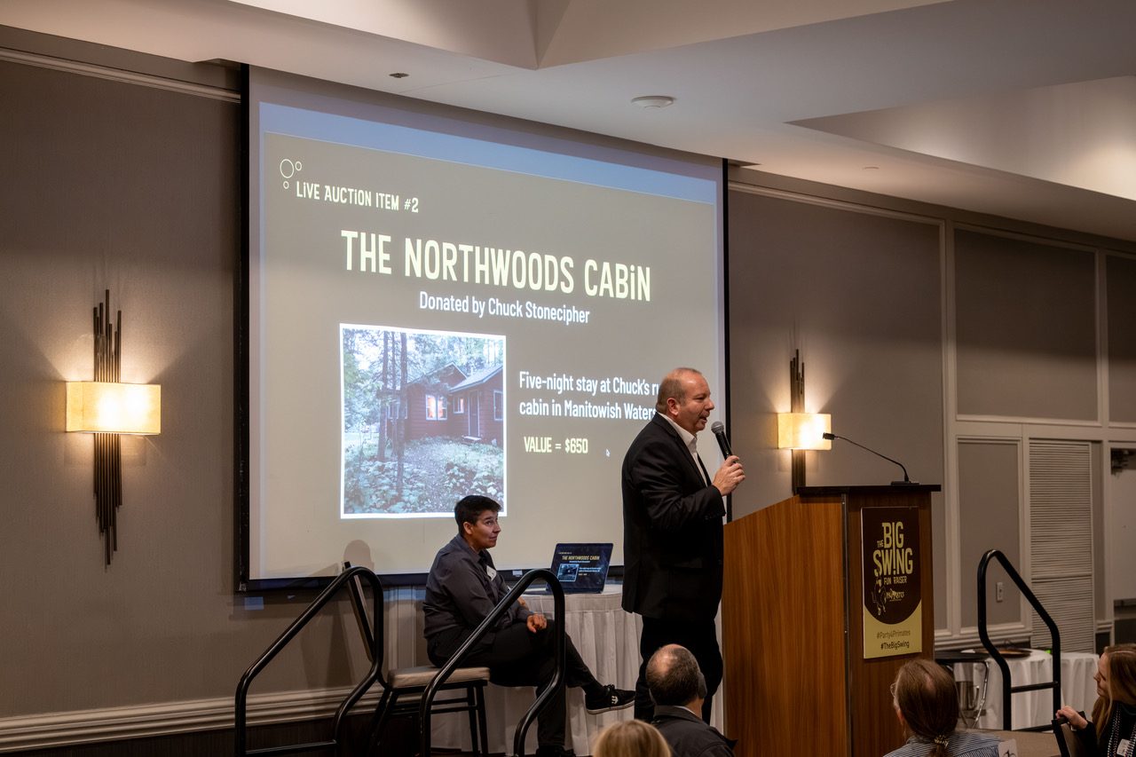 Benefit auctioneer Geoffrey Sandler at the podium calling a Northwoods cabin live auction item at Primates Incorporated's Big Swing