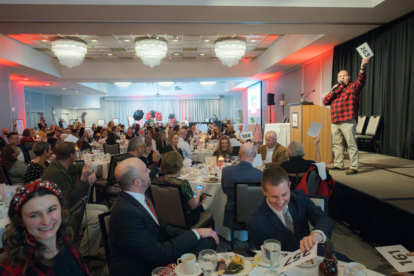 Wide view of a full gala ballroom as benefit auctioneer Geoffrey Sandler presents a live auction item from the stage at the Do Good Gala